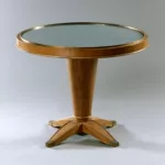Guéridon du salon de musique de première classe du paquebot Liberté, réalisé vers 1950, composé d’un fût central conique en bouleau de Norvège, de quatre pieds à sabots et d’un plateau circulaire couvert d’un textile bleu-gris sous plaque de verre.