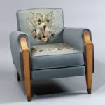 Fauteuil confortable du salon de musique de première classe du paquebot Liberté, réalisé vers 1950, avec tapisserie d’Aubusson à décor floral sur fond bleu-gris, accotoirs et piètement en bouleau de Norvège terminés par des sabots métalliques.
