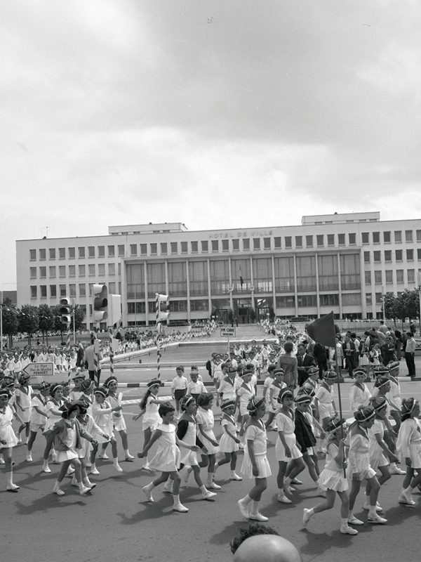 Enfants défilant devant l'hôtel de ville lors d'une kermesse en 1960