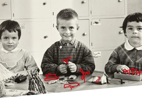Photographie en noir et blanc de trois jeunes élèves attablés en train de participer à des jeux de construction.
