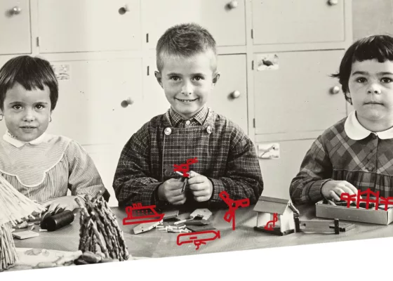 Création : Maelwenn Leduc. Photographe : Paul Lemasson. Collection Saint-Nazaire Agglomération Tourisme – Écomusée. Photographie en noir et blanc de trois jeunes élèves attablés en train de participer à des jeux de construction.