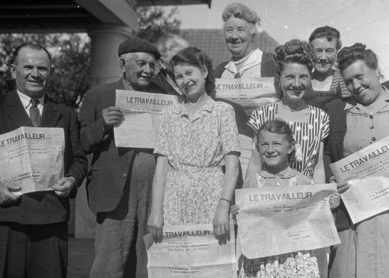 Photographie d'hommes, femmes et d'une petite fille posant avec la une du journal Le Travailleur de l'Ouest à Saint-Nazaire.