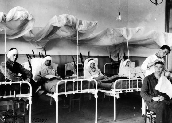 Quatre soldats alités avec un bandage autour de la tête dans une salle dédiée aux affections des oreilles alors qu'un autre se fait examiner par un médecin sur une chaise à l'hôpital de Saint-Nazaire pendant la Première Guerre mondiale..