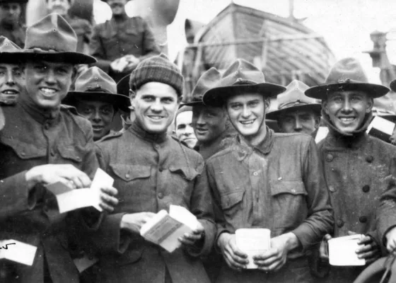 Groupe de jeunes soldats américains souriant, une boîte à tabac dans les mains devant une embarcation de sauvetage.