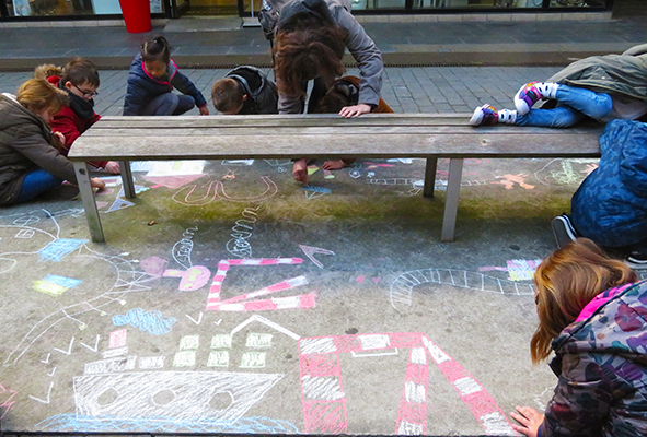 Jeunes élèves de primaire dessinant à la craie sur le sol dans la ville près du centre commercial le Paquebot.