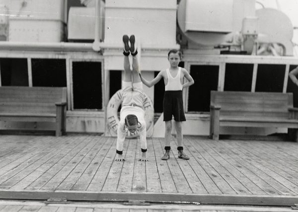 Un jeune garçon, aidé par un autre enfant, fait le poirier sur le Sun deck du paquebot Ile-de-France, le 28 juillet 1933.