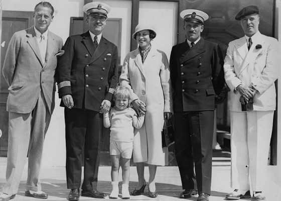 Deux hommes, une femme et un enfant posent avec le capitaine et un officier sur le pont du paquebot Ile-de-France, le 28 juillet 1933.