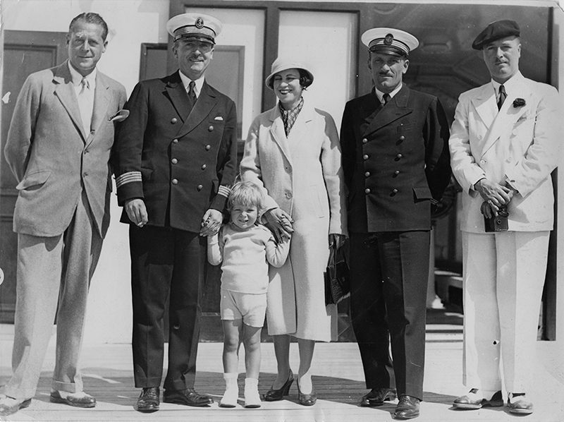Deux hommes, une femme et un enfant posent avec le capitaine et un officier sur le pont du paquebot Ile-de-France, le 28 juillet 1933.