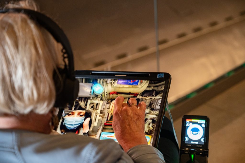 Femme assise dans un fauteuil roulant de dos avec une tablette numérique dans les mains.