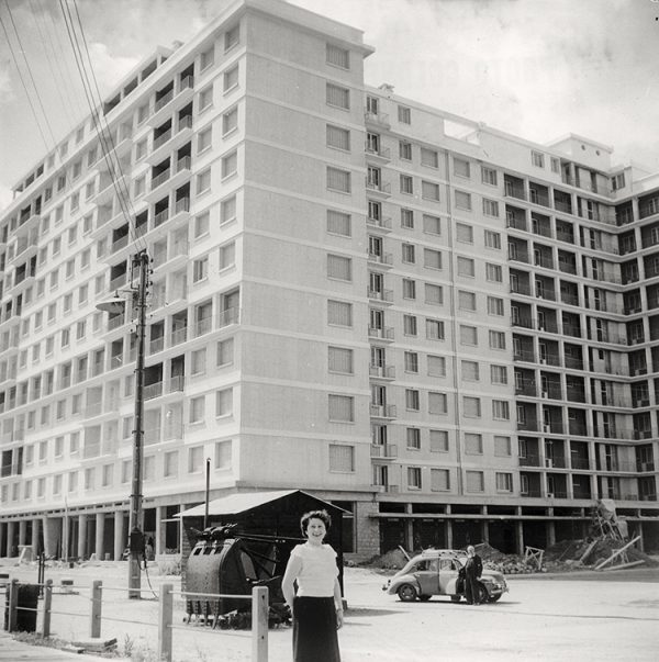 Femme posant au pied du Building en construction vers 1953.