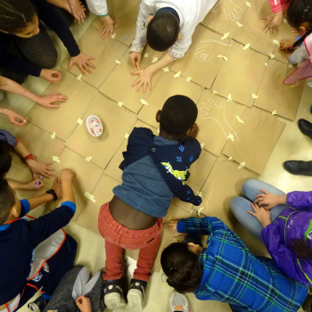 Jeunes élèves de primaire vus du dessus en train de dessiner le contour de leur main sur des cartons au cours d'une action pédagogique.