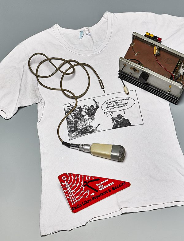 Tee-shirt blanc sur lequel sont posés un émetteur radio, un micro et un autocollant de la Radio Libre Populaire de Saint-Nazaire.