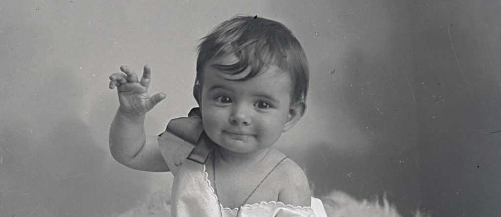 Portrait d'un bébé faisant un geste de la main en direction de l'objectif dans un studio du début du 19ème siècle.