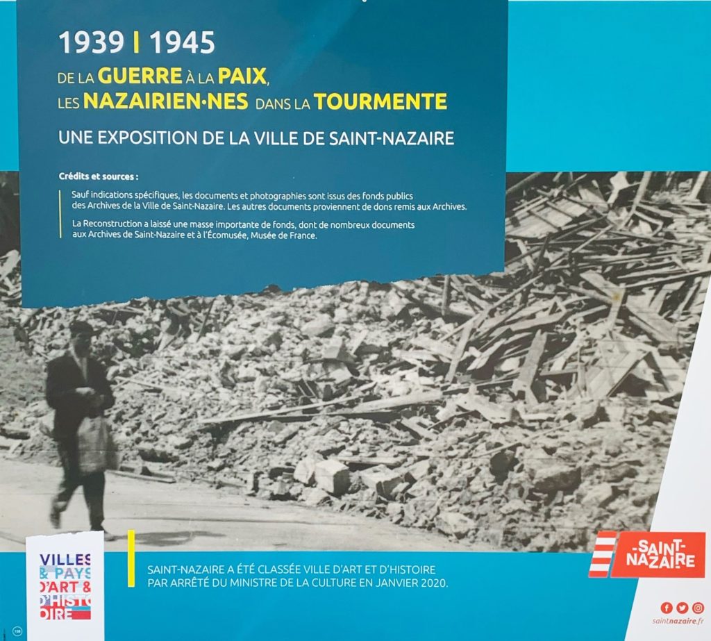 Premier panneau de l'exposition "1939-1945, de la guerre à la paix, les Nazairiens dans la tourmente" avec une photographie d'un homme marchant dans les ruines de Saint-Nazaire après la Seconde Guerre mondiale.