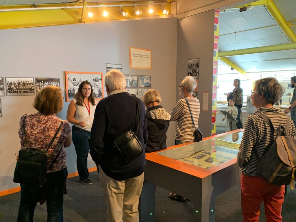 Groupe de visiteurs devant une médiatrice dans la salle d'exposition de l'Écomusée