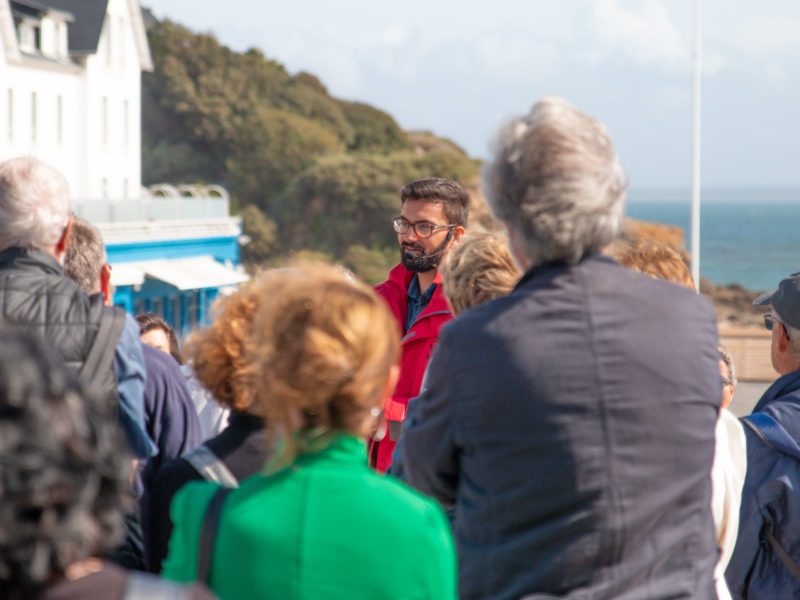 Guide s'adressant à un groupe de visiteurs lors d'une visite guidée devant l'hôtel de la plage à Saint-Marc-sur-Mer.