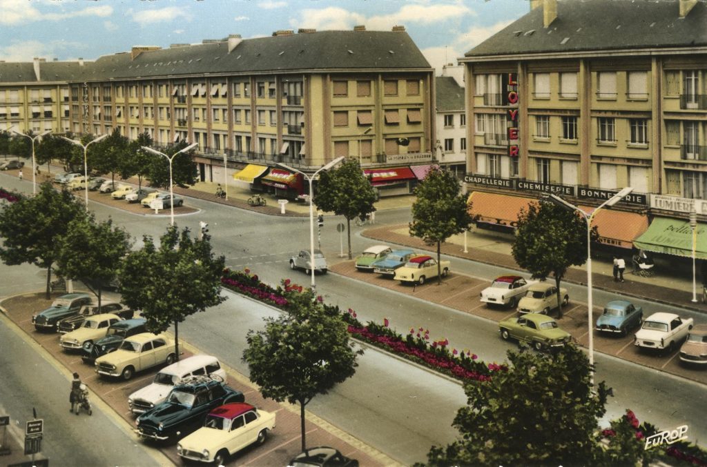 Carte postale colorisée représentant une vue aérienne de l'avenue de la République avec immeubles et places de parking à Saint-Nazaire.