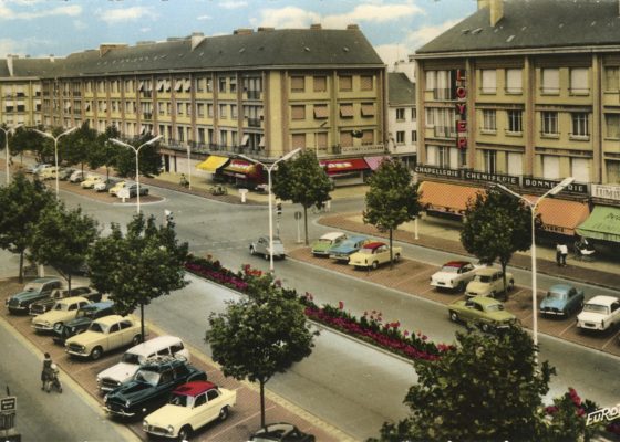 Carte postale colorisée représentant une vue aérienne de l'avenue de la République avec immeubles et places de parking à Saint-Nazaire.