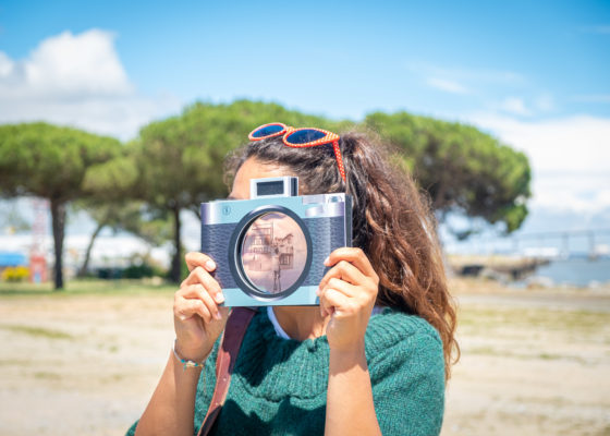 Jeune femme dont le visage est caché par un faux appareil photographique au bord de l'estuaire à Saint-Nazaire.