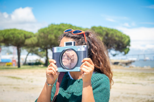 Jeune femme dont le visage est caché par un faux appareil photographique au bord de l'estuaire à Saint-Nazaire.