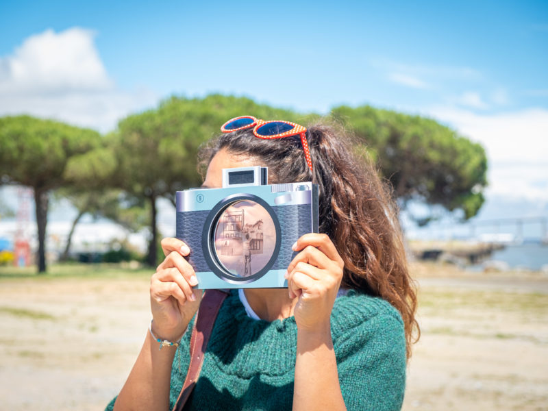 Jeune femme dont le visage est caché par un faux appareil photographique au bord de l'estuaire à Saint-Nazaire.