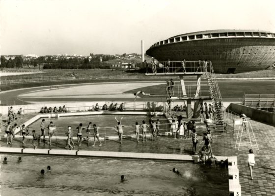 Photographe : Paul Lemasson. Architectes : Louis Longuet, René Rivière et Roger Vissuzaine. Collection Saint-Nazaire Agglomération Tourisme-Écomusée Photographie noir et blanc représentant une vue aérienne de deux bassins extérieurs de la piscine Léo Lagrange avec de nombreux baigneurs devant la Soucoupe.