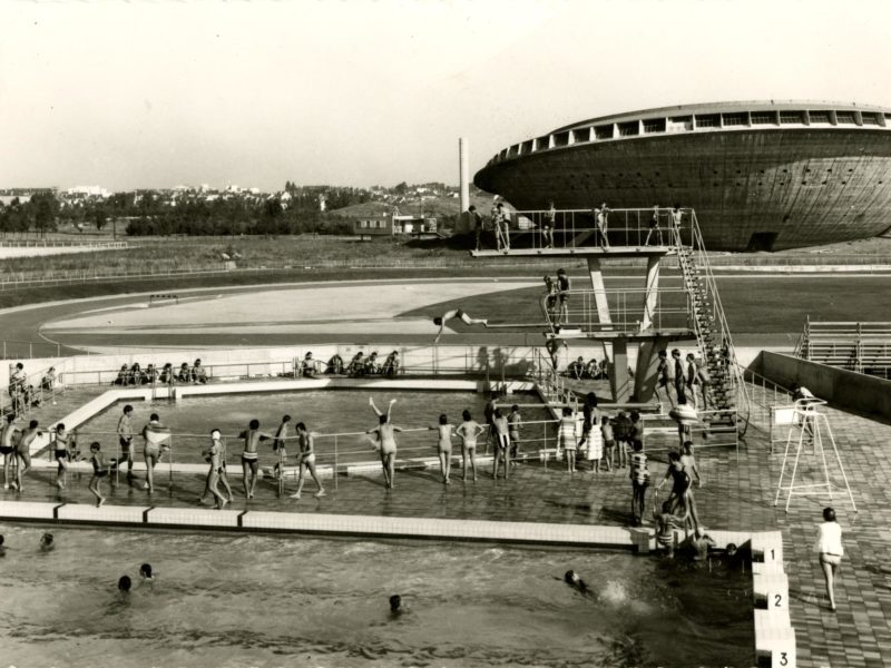 Photographie noir et blanc représentant une vue aérienne de deux bassins extérieurs de la piscine Léo Lagrange avec de nombreux baigneurs devant la Soucoupe.