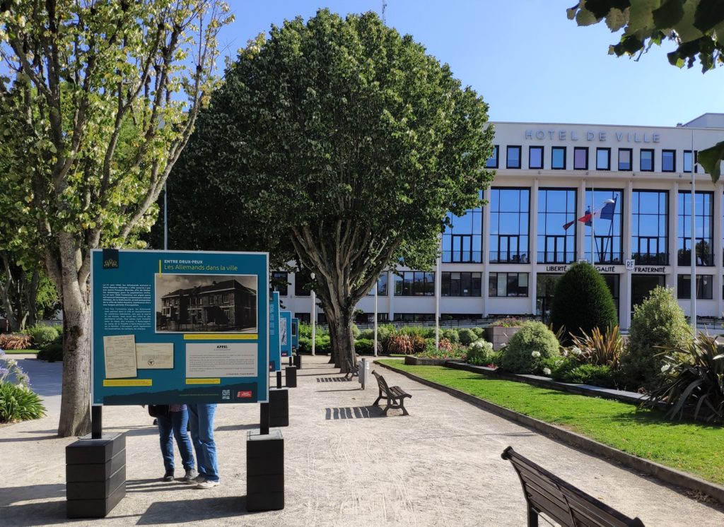 Panneau de l'exposition sur la Seconde Guerre mondiale avec derrière la façade de l'hôtel de ville de Saint-Nazaire