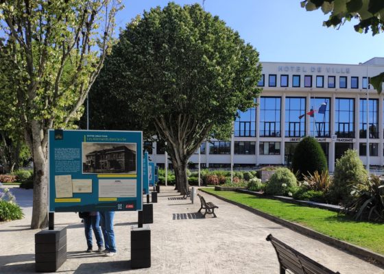 Photographe : Éloïse Bugeau Panneau de l'exposition sur la Seconde Guerre mondiale avec derrière la façade de l'hôtel de ville de Saint-Nazaire