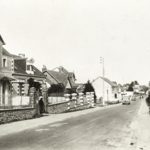 Carte postale noir et blanc représentant une rue en pente de Saint-Nazaire où circulent deux voitures dans les années 1930.