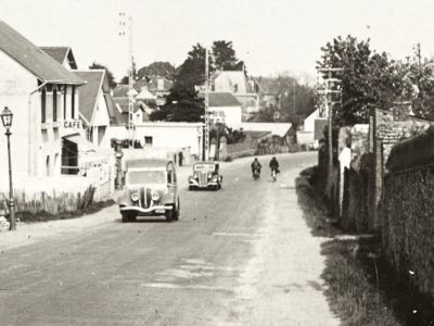 Détail d'une carte postale noir et blanc représentant un café de Saint-Nazaire avec deux voitures dans les années 1930.