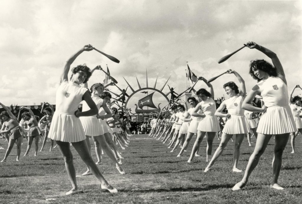 Photographie en noir et blanc montrant de très nombreuses gymnastes prenant une pose en forme d'arc de cercle, une quille à la main dans un stade. Le Plessis est un des sujets mis à l'honneur pour les Journées du Patrimoine 2020.