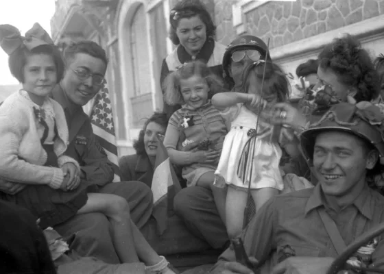 Photographie en noir et blanc représentant des soldats américains posant sur une jeep avec des enfants et des jeunes femmes à la Libération.