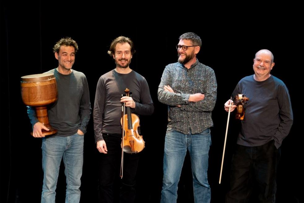 Trois musiciens et un anthropologue sont photographiés de face en rigolant.