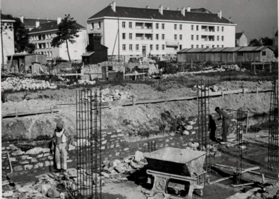 Photographie noir et blanc représentant des hommes construisant une maison devant les HLM du quartier Gambetta à Saint-Nazaire évoqué dans une visite des Journées du Patrimoine.