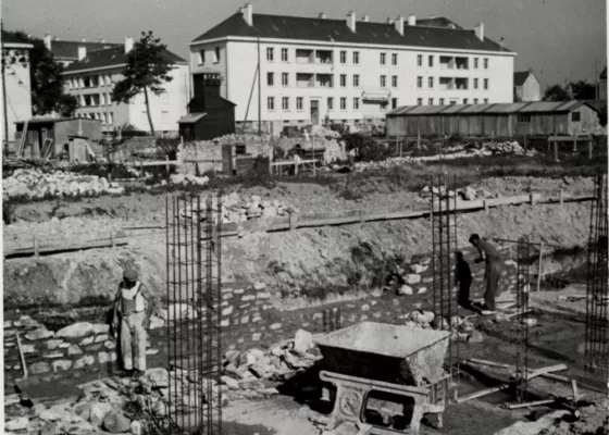 Photographie noir et blanc représentant des hommes construisant une maison devant les HLM du quartier Gambetta à Saint-Nazaire évoqué dans une visite des Journées du Patrimoine.