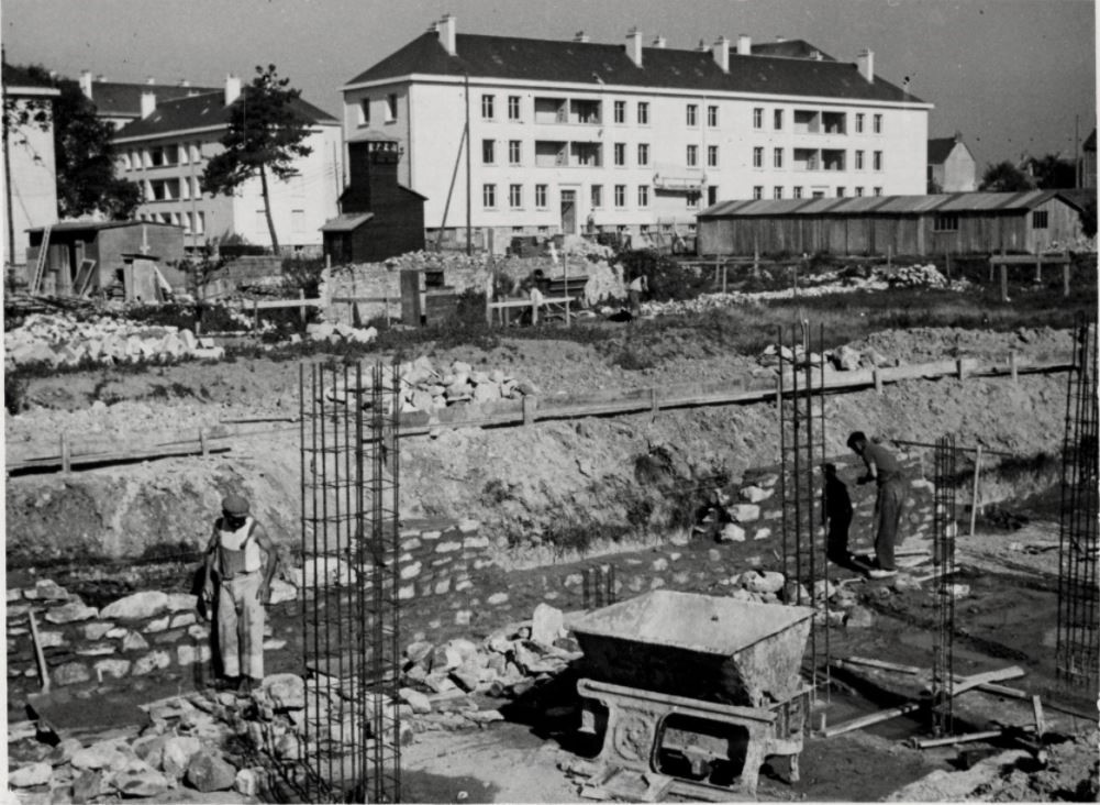 Photographie noir et blanc représentant des hommes construisant une maison devant les HLM du quartier Gambetta à Saint-Nazaire évoqué dans une visite des Journées du Patrimoine.