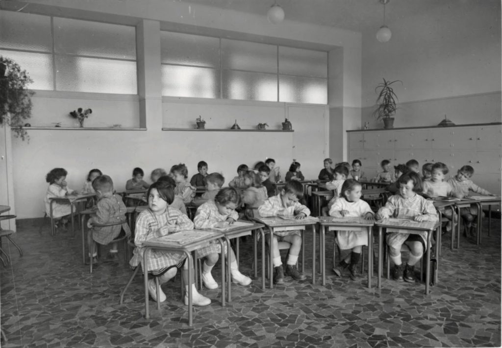 Photographie noir et blanc de maternels attablés dans leur salle de classe pour illustrer la visite de l'école moderne pour les Journées du Patrimoine.