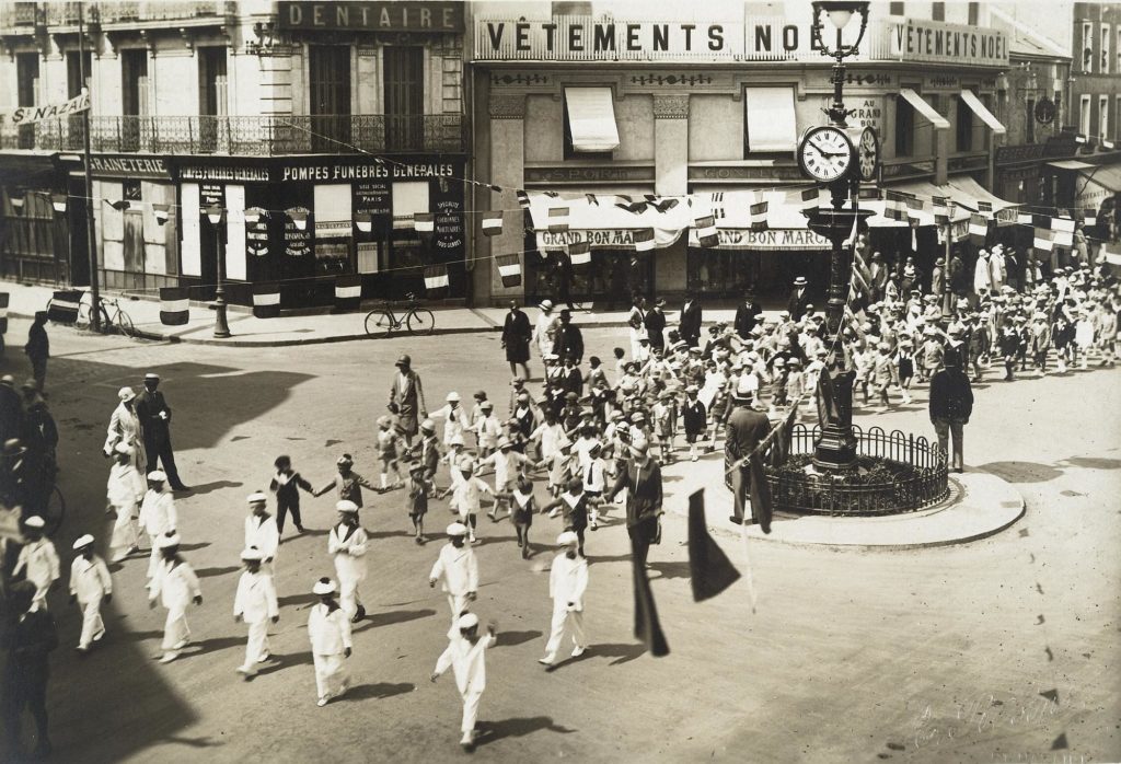 Photographie noir et blanc d'un défilé d'enfants déguisés en matelots sur la place Carnot pavoisée.