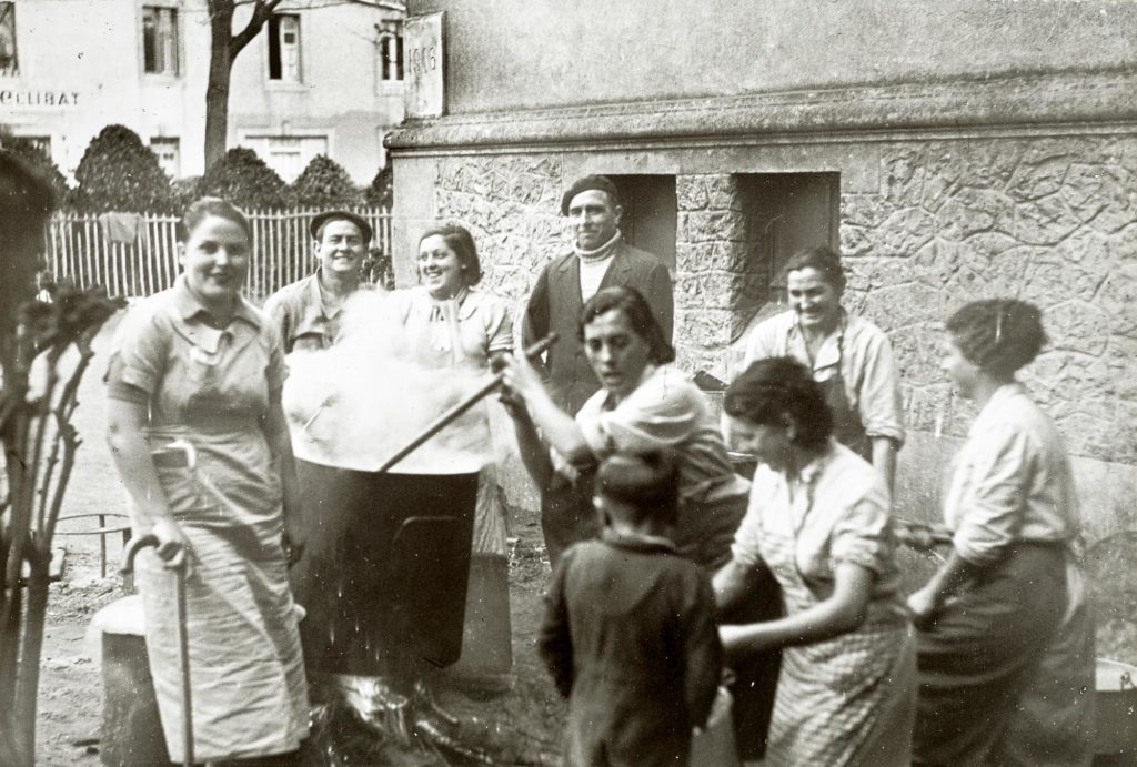 Photographie noir et blanc de réfugiés espagnols avec des hommes, des femmes et un enfant rassemblés autour d'une grande marmite devant l'hôtel du célibat.