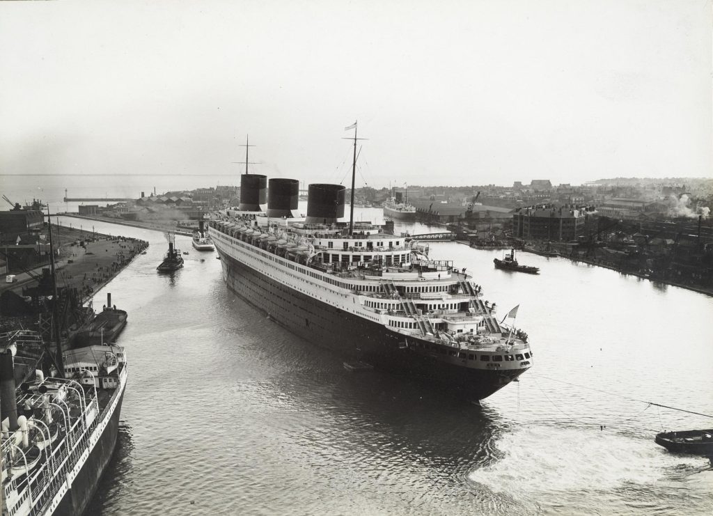 Photographie aérienne en noir et blanc représentant le paquebot Normandie dans un bassin du port de Saint-Nazaire.