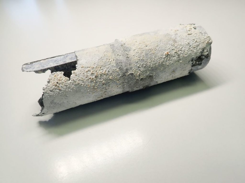 Photographie d'une cartouche métallique fortement oxydée et présentant des restes de ciment.