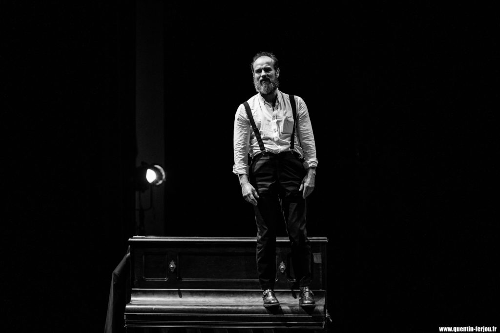 Photographie en noir et blanc d'un homme se tenant debout sur scène.