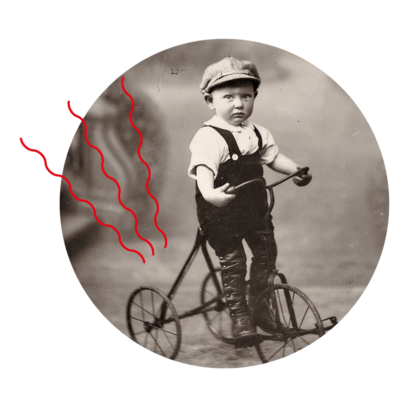 Photographie noir et blanc prise en studio d'un bébé sur un tricycle.