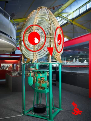 Photographie d'une lanterne de phare dans la salle de l'Écomusée sur laquelle ont été rajouté des yeux et un bec simulant une tête de chouette en référence à l'activité famille "Tout petit, si grand".