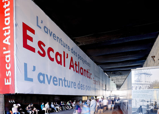 Entrée d'Escal'Atlantic dans la base sous-marine avec une bâche recouvrant le mur et présentant le musée. Devant de nombreux visiteurs.