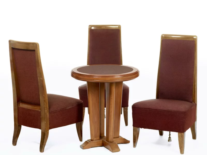 Décorateur : Le Bûcheron. Collection Saint-Nazaire Agglomération Tourisme - Écomusée. Cliché Jean-Claude Lemée Trois chaises et une table de jeu ronde en bois et tissu bordeaux.