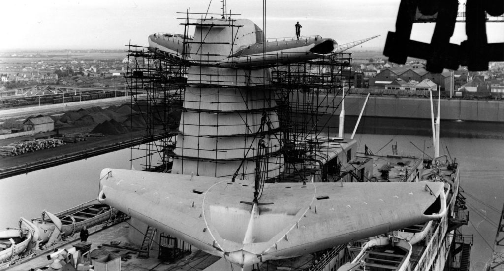Photographie noir et blanc prise depuis une grue représentant le pont supérieur du paquebot France lors de la pose des ailerons de l'une des deux cheminées.