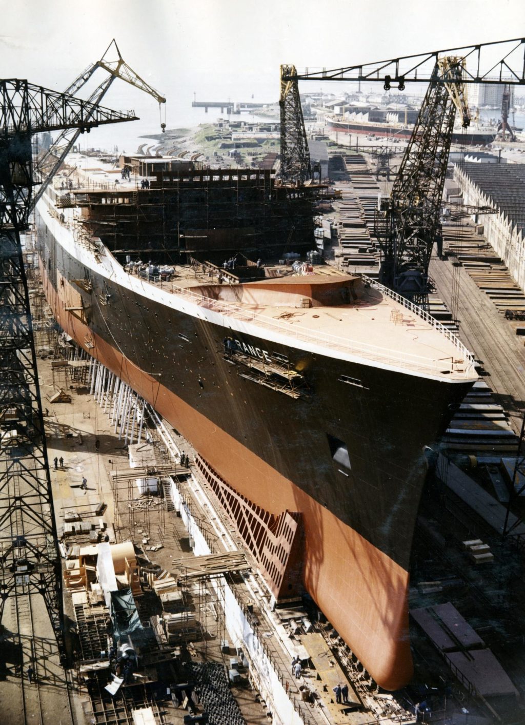 Vue aérienne en couleur du paquebot France en cours de construction, la coque est déjà peinte et il est entouré de 4 grues.