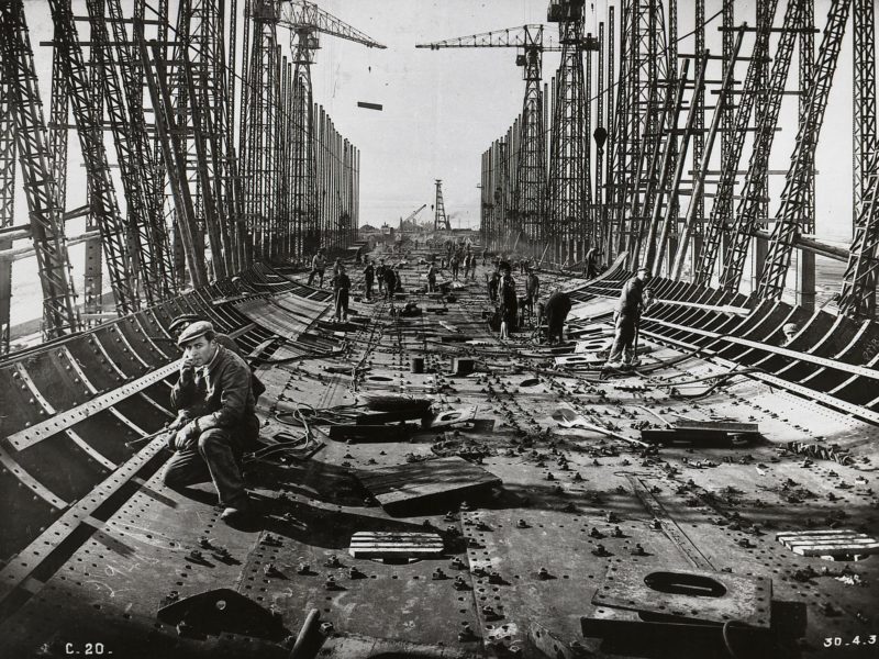 Photographie noir et blanc d'ouvriers travaillant au rivetage de la coque du paquebot Normandie en 1931.